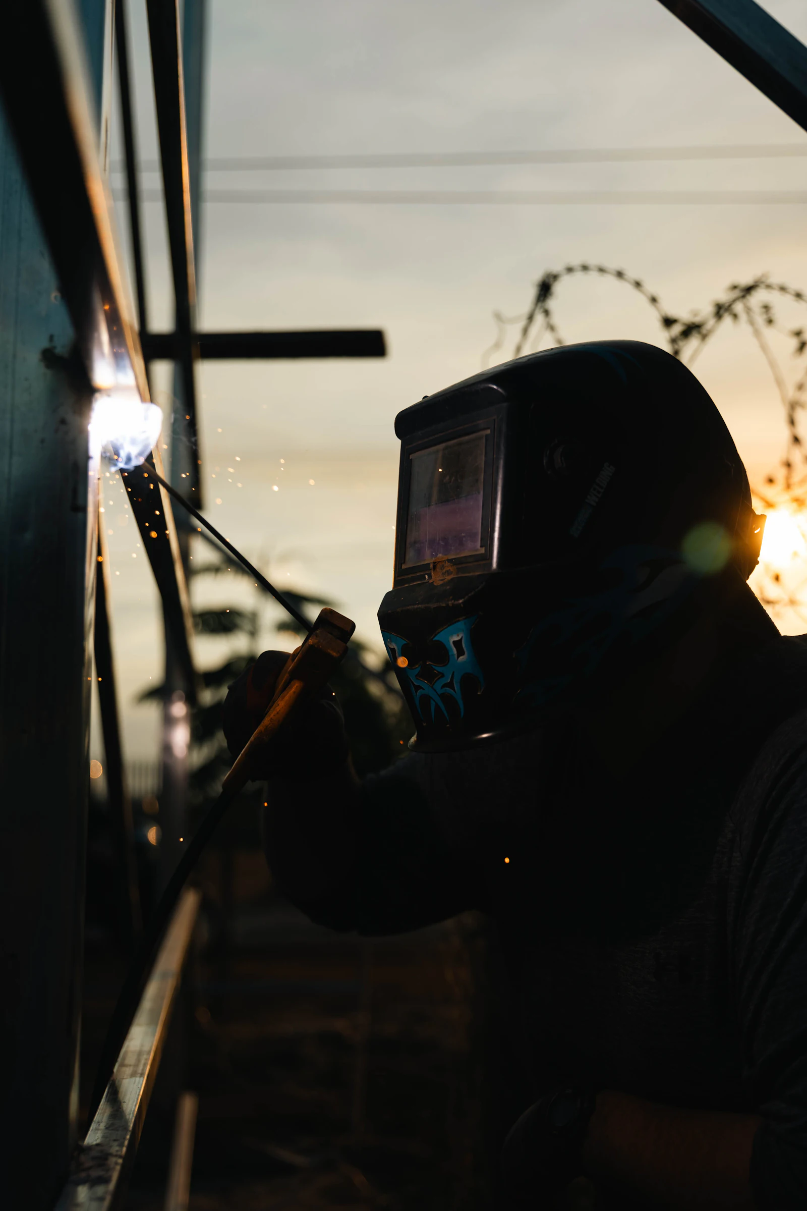 Saldatore con maschera al lavoro in cantiere al tramonto